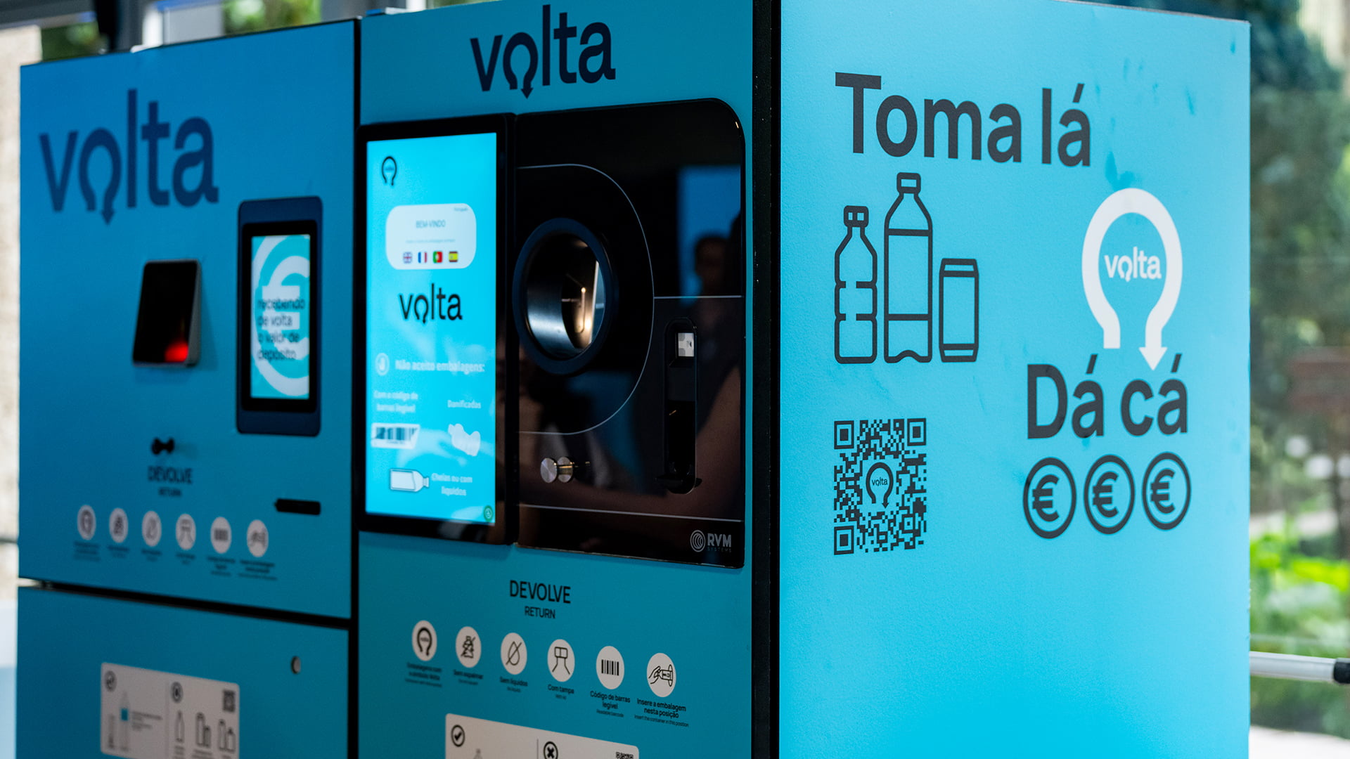 Máquina Volta de devolução de embalagens colocada junto a um edifício com um parque ao fundo